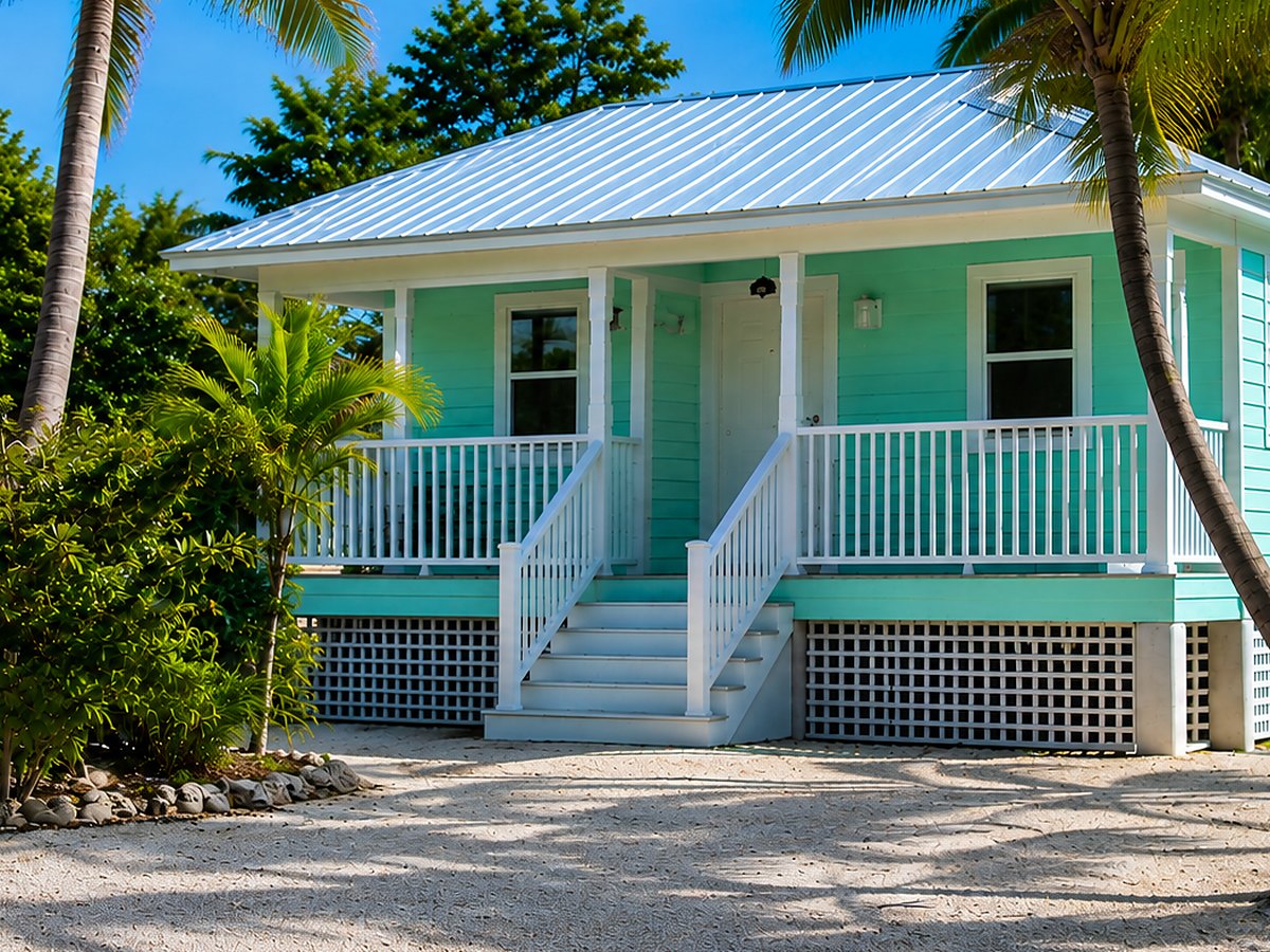 A raised Islamorada cottage with a metal roof, front porch, and lattice skirting on a crushed-rock lot